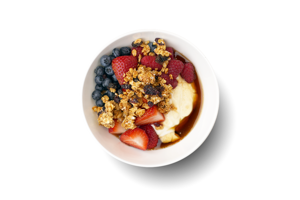 An overhead photo of a fruit, granola, honey, and yogurt parfait bowl.
